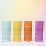 Load image into Gallery viewer, Nöz sunscreen stick packages in purple, orange, yellow and blue in front of a gradient background
