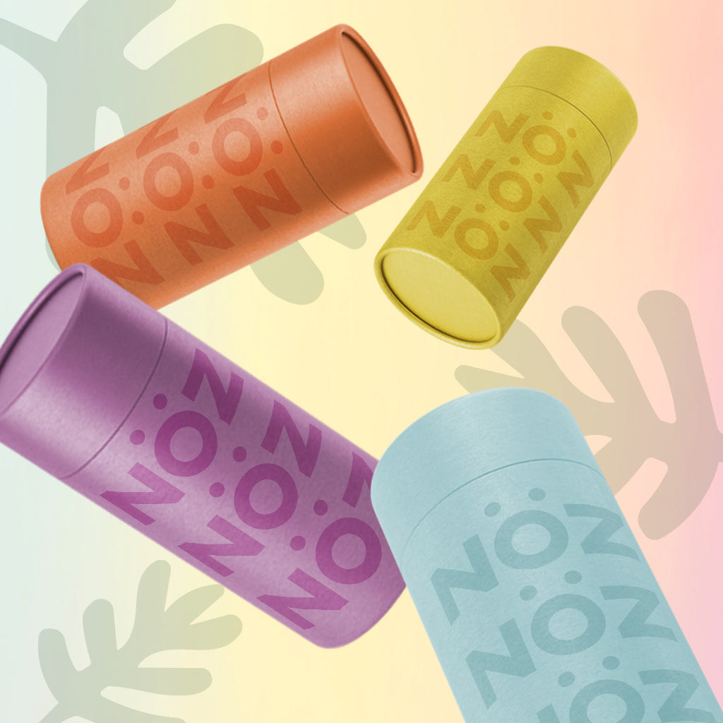 Nöz sunscreen stick packages in purple, orange, yellow and blue in front of a gradient background with leaf graphics