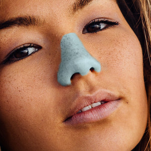 A woman with freckles wearing blue Nöz sunscreen on her nose