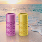 Load image into Gallery viewer, A purple and a yellow stick of Nöz sunscreen on the beach at sunset
